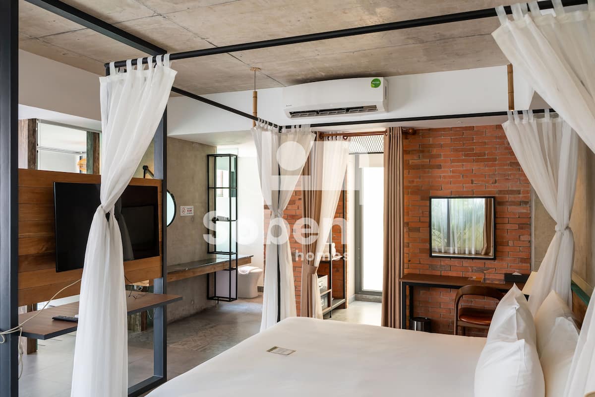 A modern hotel room with a large bed, a TV, a desk, and a brick wall.