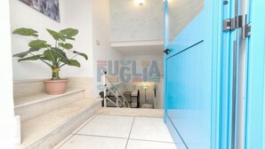 Unes escales condueixen a una habitació amb una porta blava, una planta en test i un mur amb la inscripció 'PUGLIA ONLINE'.