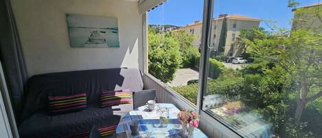 A balcony with a view of a residential area, a table with a tablecloth, a chair, a couch, and a painting on the wall.