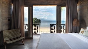 Ein Schlafzimmer mit einem großen Bett, einer Bank und Blick auf Strand und Wasser.
