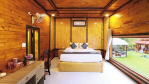 A wooden cabin bedroom with a bed, bedside table, and a window with a view of an outdoor area.