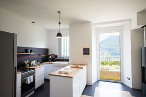 A modern kitchen with a central island, a stove, and a sink. There is a balcony with a view of the mountains. - Up & Up - MyHomeinComo (Moltrasio)