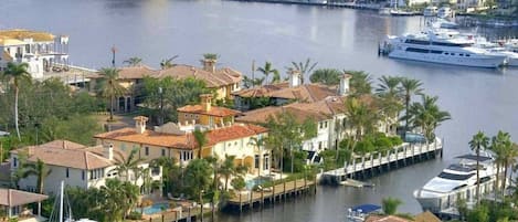 A marina with several docked boats, a waterfront property with a pool, and a backdrop of urban buildings.
