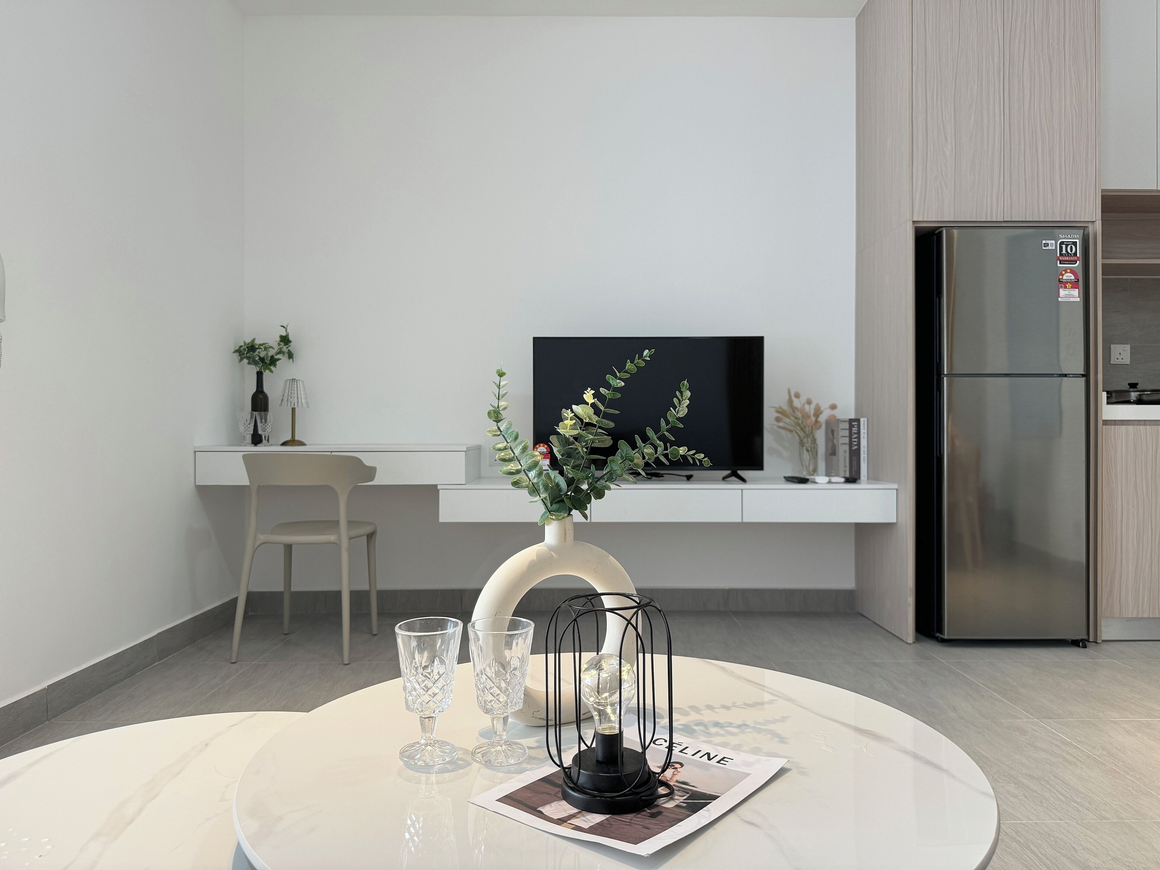 A modern kitchen with a built-in refrigerator, a dining area with a round table, and a TV mounted on the wall.