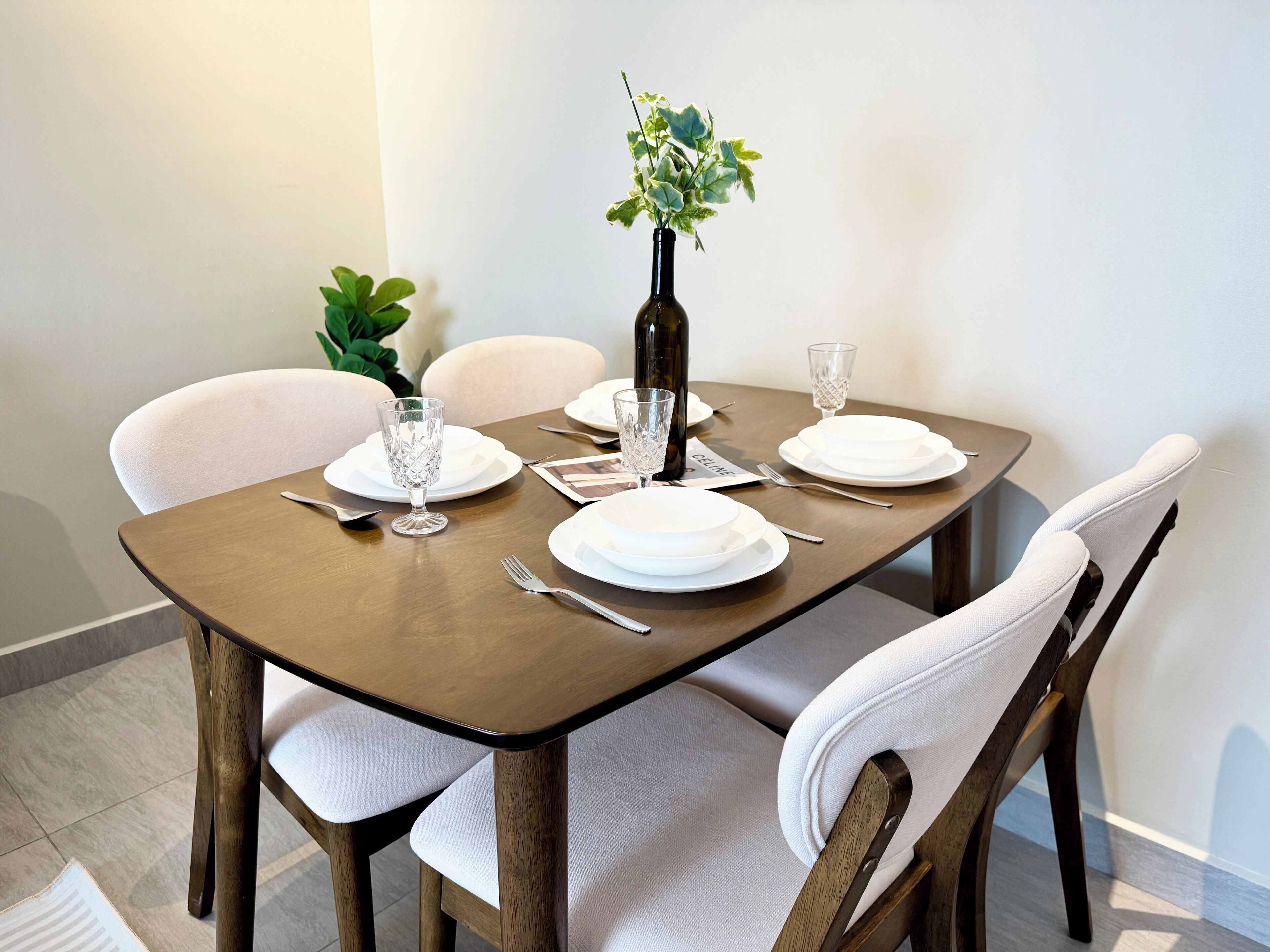 A dining table set with white plates, silverware, and crystal glasses, surrounded by upholstered chairs.