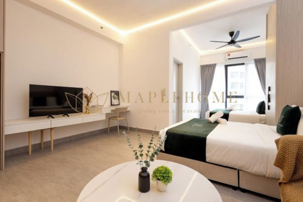 Une chambre d’hôtel moderne équipée d’un lit, d’un bureau avec une télévision, d’un ventilateur de plafond et d’une petite plante posée sur une table ronde.