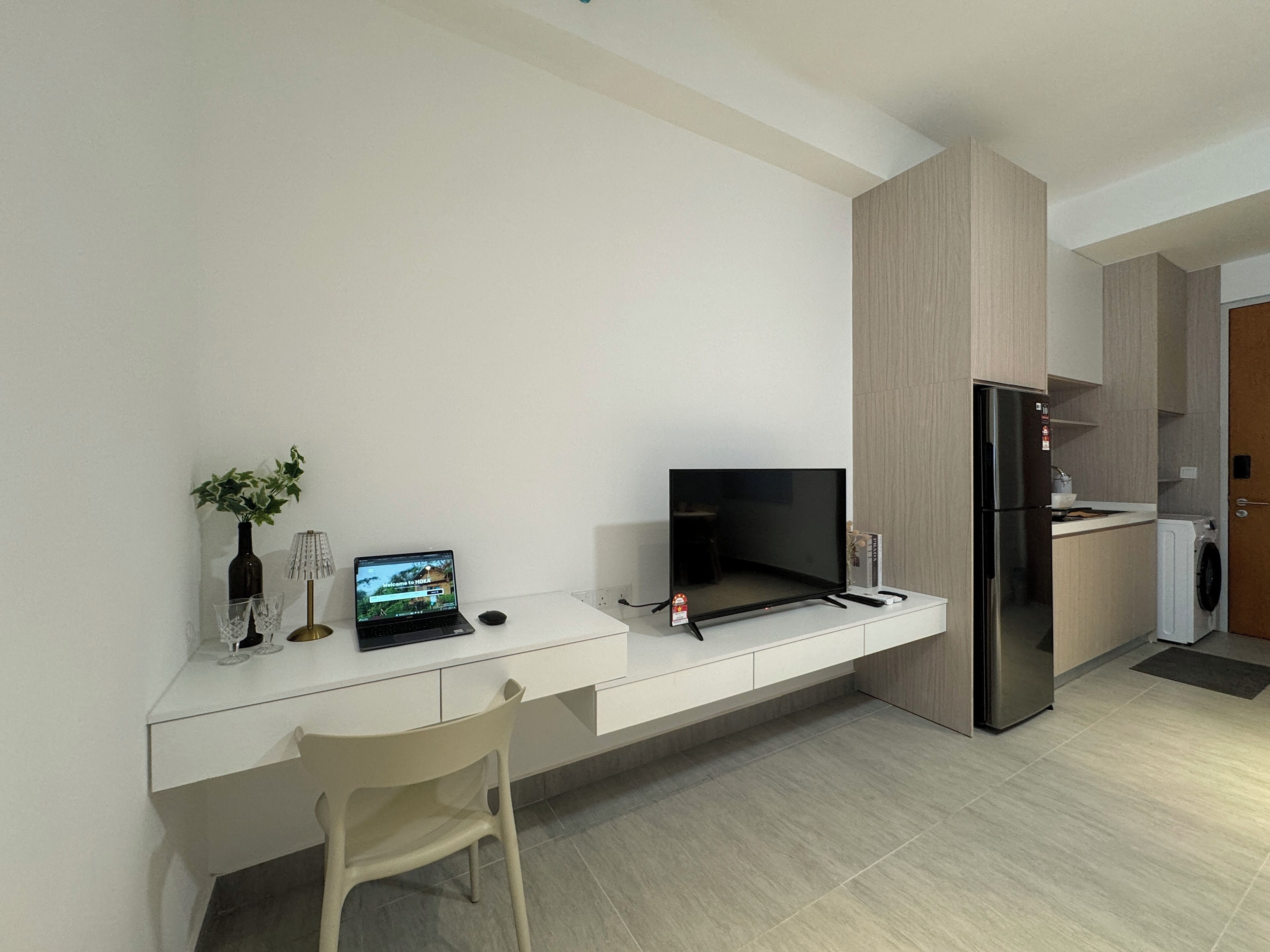 A modern kitchen with a built-in desk, a flat-screen TV, and a stainless steel refrigerator.
