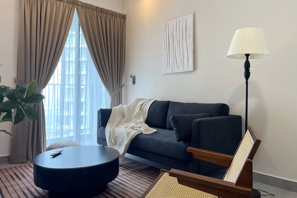 A modern living room with a dark sofa, a round coffee table, a floor lamp, and a large window with curtains.