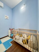 A baby room with a wooden crib, toys, a play mat, and a wall-mounted air conditioner.