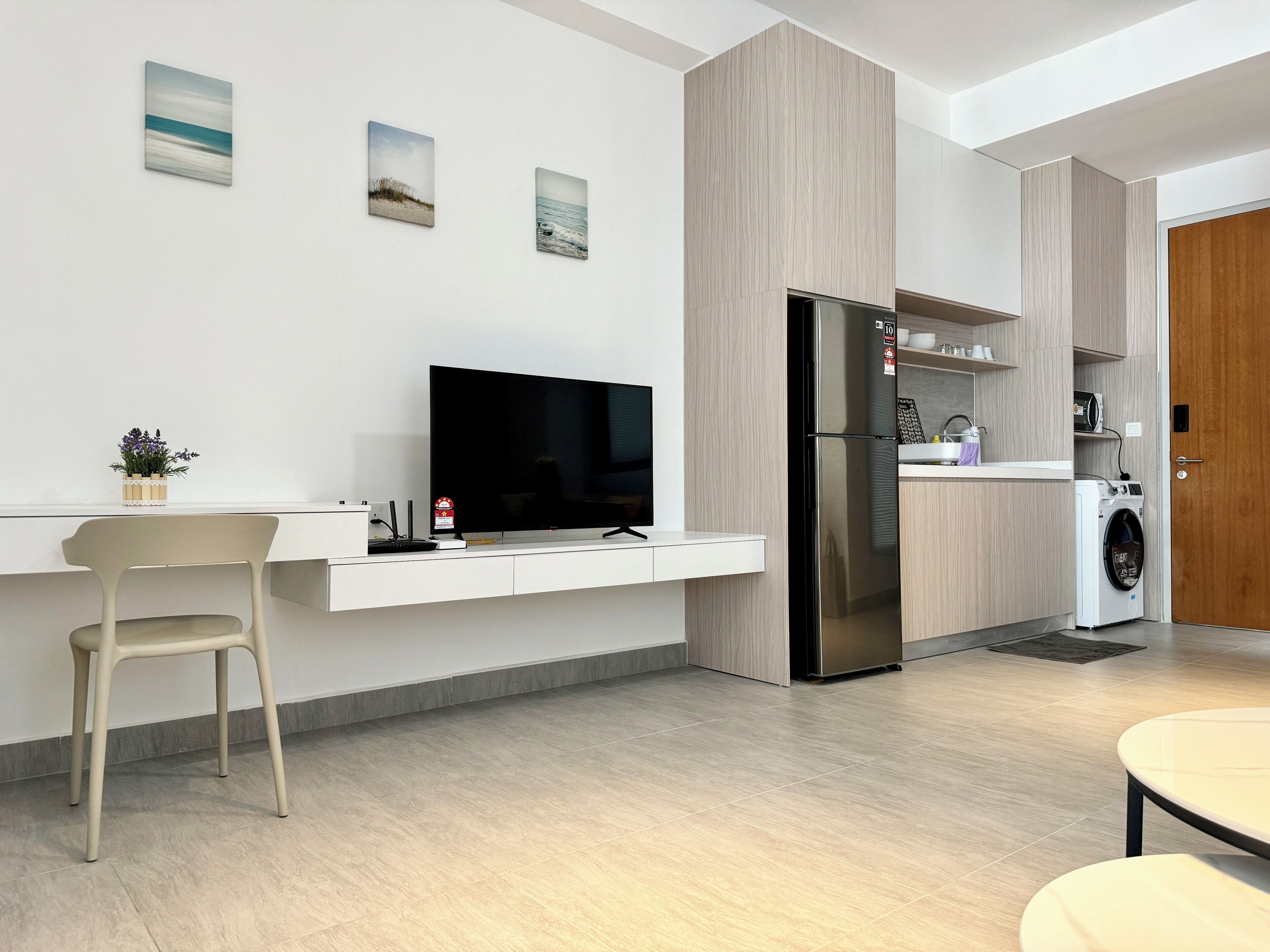 A modern kitchen with a built-in refrigerator, a microwave, and a washing machine. There is a dining table and a chair in the center of the room.