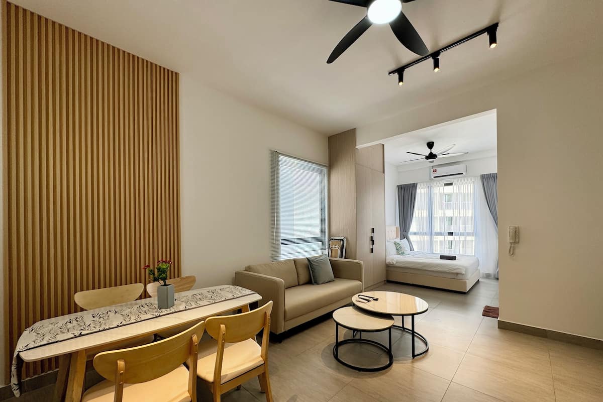A modern living room with a sofa, a dining table with chairs, a ceiling fan, and a bed in the background.
