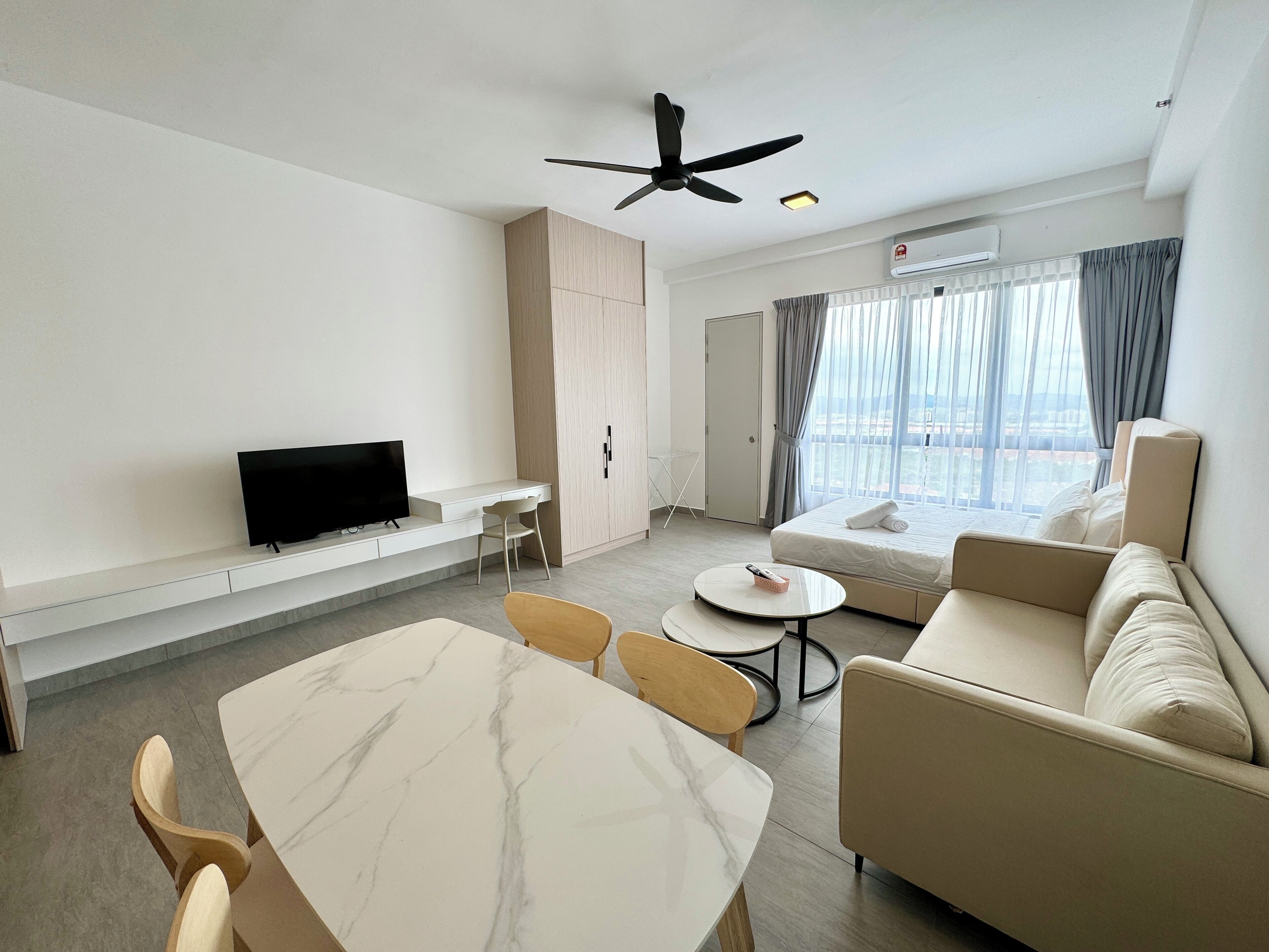 A modern hotel room with a flat-screen TV, a dining table, a sofa, and a ceiling fan.