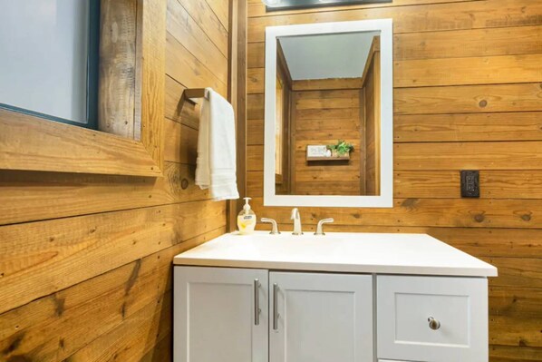 Un baño con paneles de madera, un tocador blanco, un espejo y un pequeño estante con una planta.