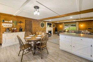 Una cocina amplia con paredes de madera, un comedor con una mesa redonda y una sala de estar con sofá y chimenea.
