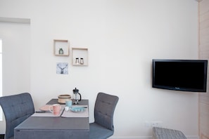 Una sala de estar moderna con una mesa de comedor, dos sillas, un televisor y adornos en la pared.