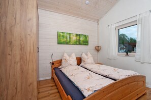 Una cama de madera con colchón azul, paredes blancas y una ventana con cortinas blancas.