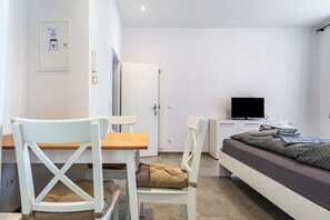 Una habitación moderna con cama, escritorio, silla, televisor y puerta.