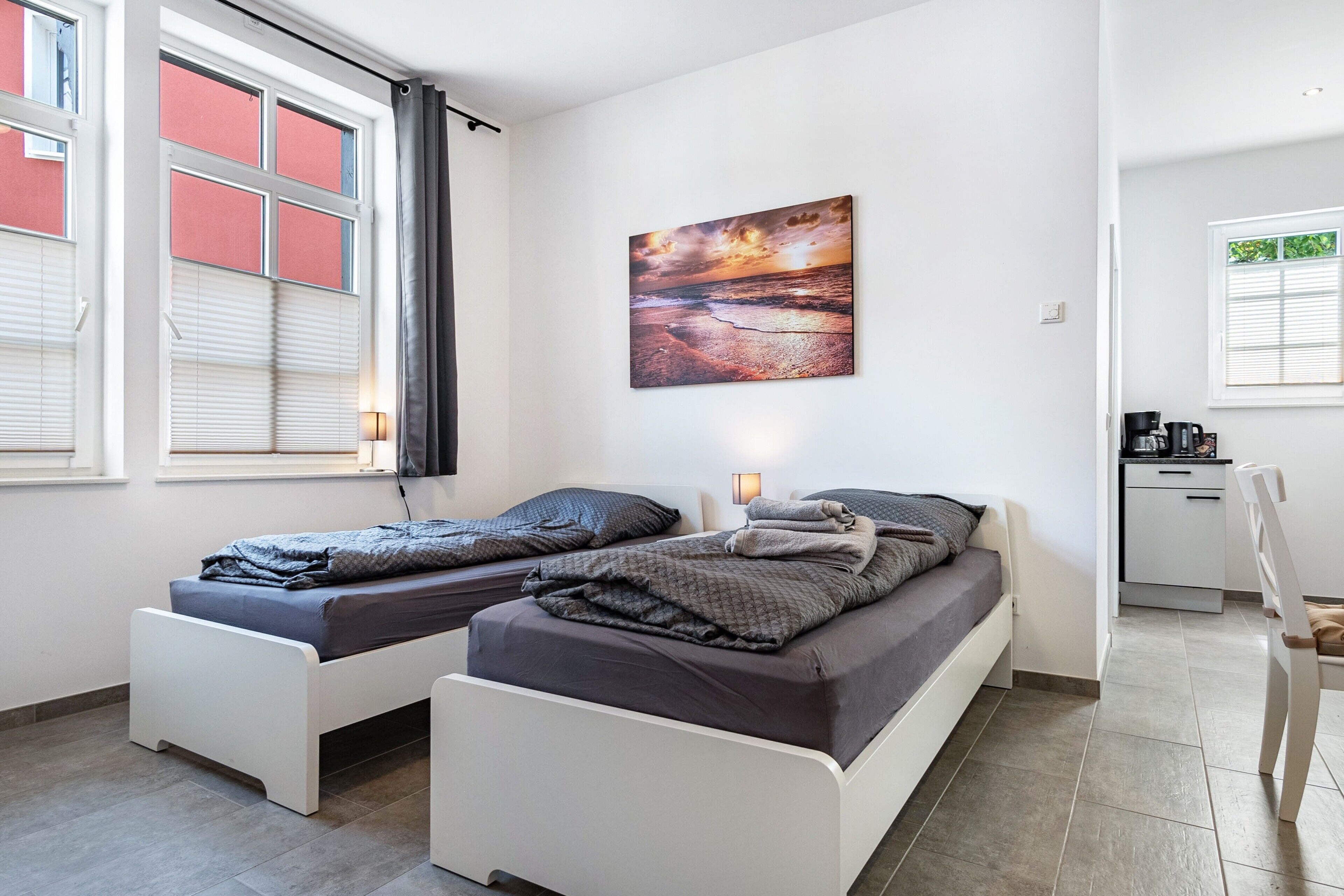 A room with two single beds, a desk, a chair, and a painting on the wall.