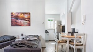 Een slaapkamer met een bed, nachtkastje, lamp en een schilderij van een zonsondergang.