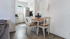 Een knus woongedeelte met een kitchenette, een eethoek met twee stoelen, een bed en een raam met zonwering.