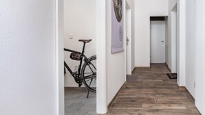 Een gang met een houten vloer, een fiets en een deur aan het einde.