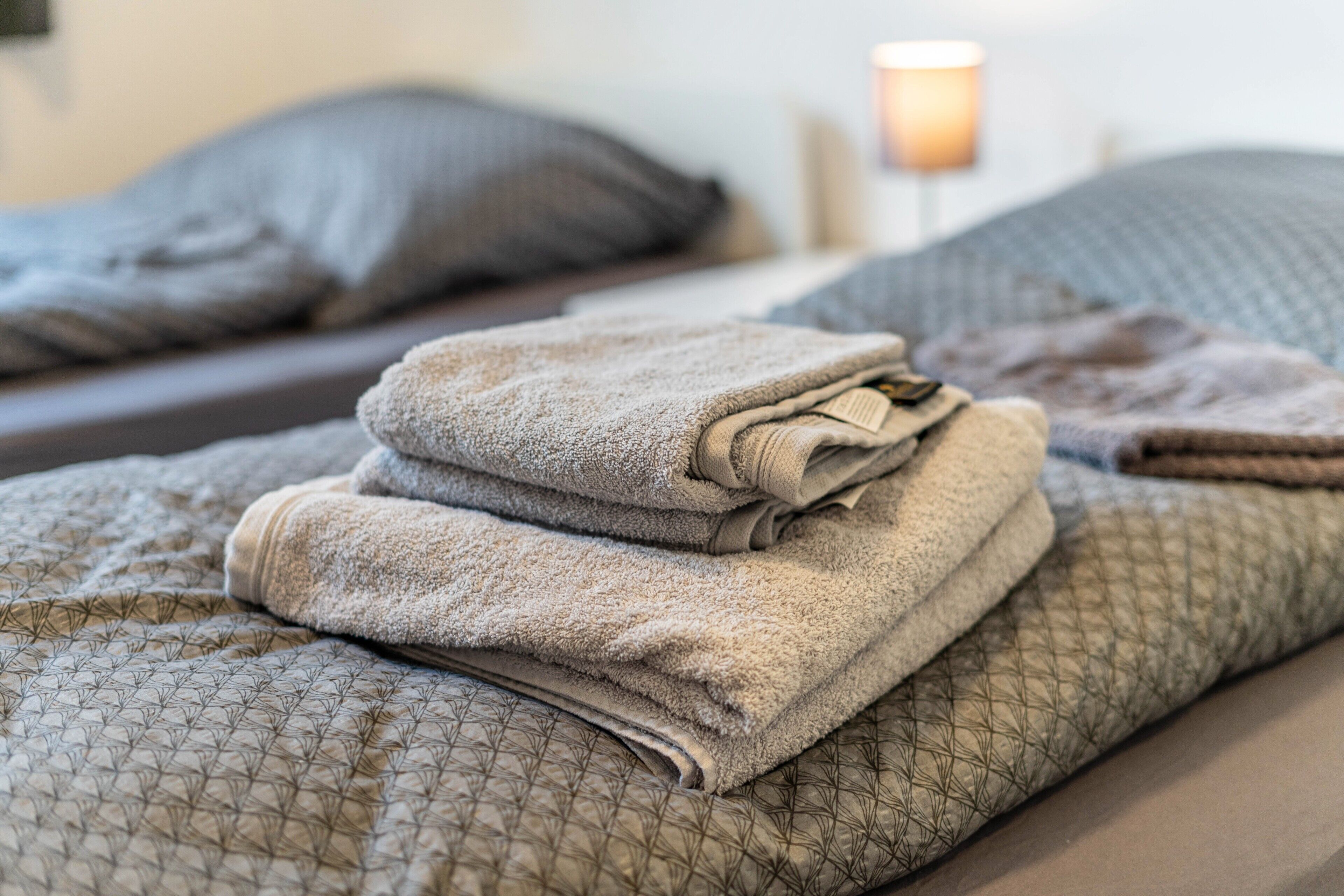A neatly made bed with folded towels and a patterned bedspread.