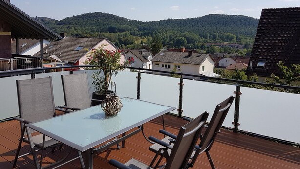 A balcony with a table and chairs, a potted plant, and a view of houses and mountains. - Apartment 'Ruth' with Private Terrace and Wi-Fi (Dahn)