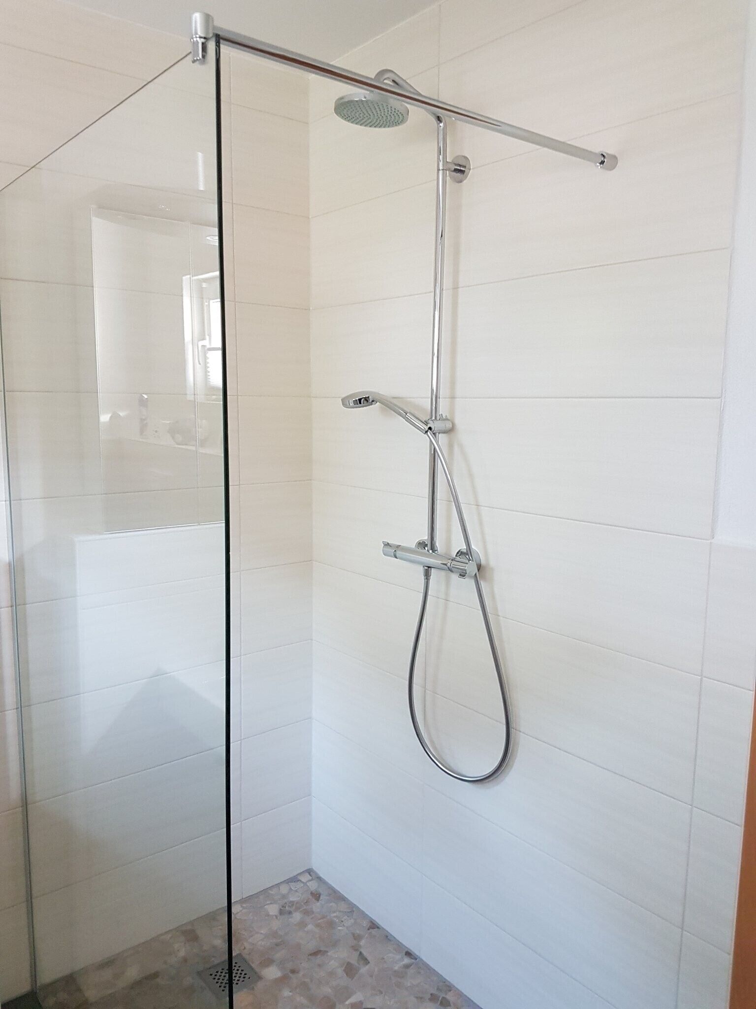 A glass-enclosed shower with a handheld showerhead and a wall-mounted faucet.