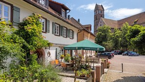 Ein traditionelles europäisches Gebäude mit Innenhof, Außenbestuhlung und einer Kirche im Hintergrund.