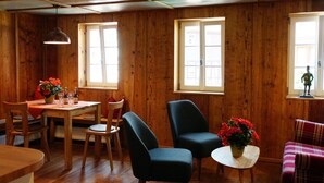 Ein Zimmer mit Holzwänden, einem Esstisch, zwei Stühlen, einem kleinen runden Tisch mit Blumenvase und einem karierten Sofa.