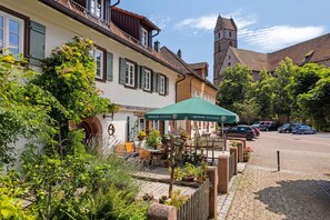 A traditional European building with a courtyard, outdoor seating, and a church in the background. - Holiday Apartment Im Denkmal 1 with Wi-Fi (Alpirsbach)