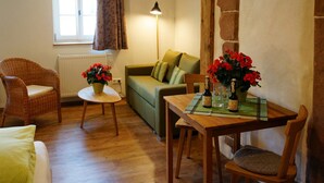 A cozy living room with a green sofa, a wicker chair, a wooden table with a bottle and glasses, and a potted plant. - Holiday Apartment Im Denkmal 1 with Wi-Fi (Alpirsbach)