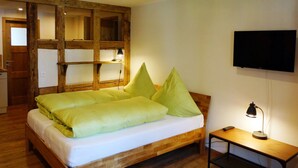A wooden bed with green pillows, a bedside table with a lamp, and a TV on the wall. - Holiday Apartment Im Denkmal 1 with Wi-Fi (Alpirsbach)