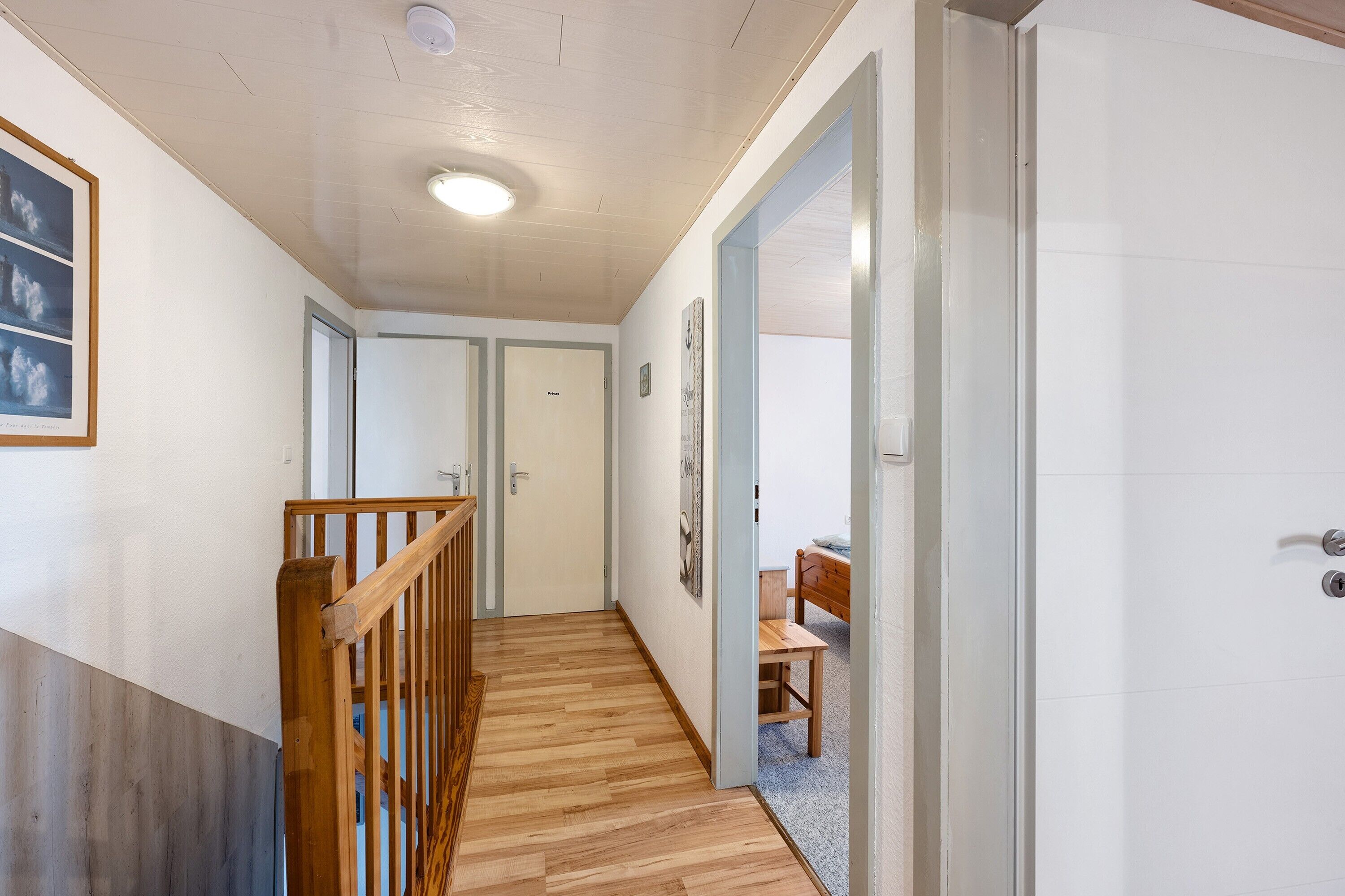 Un couloir doté d’un plancher en bois, d’une rambarde en bois et d’une porte au fond.