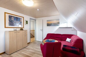 Huoneessa on puinen vaatekaappi, punainen sohva, pieni pöytä ja seinällä taulu.