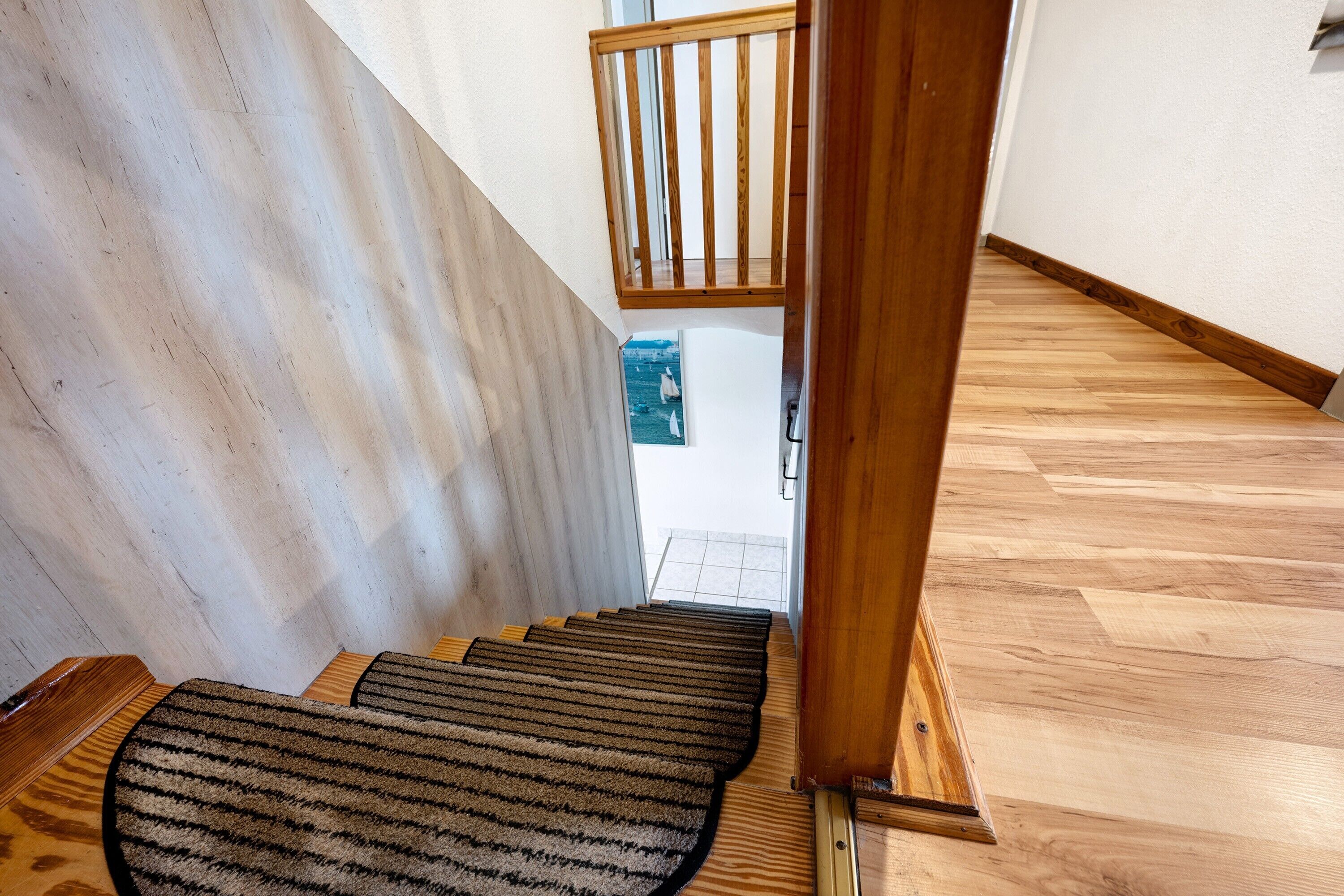 Un escalier en bois, recouvert d’une moquette à rayures, mène à un balcon.