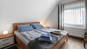 Ein Schlafzimmer mit Bett, Nachttischen, einem Sessel und einem Fenster mit Vorhängen.