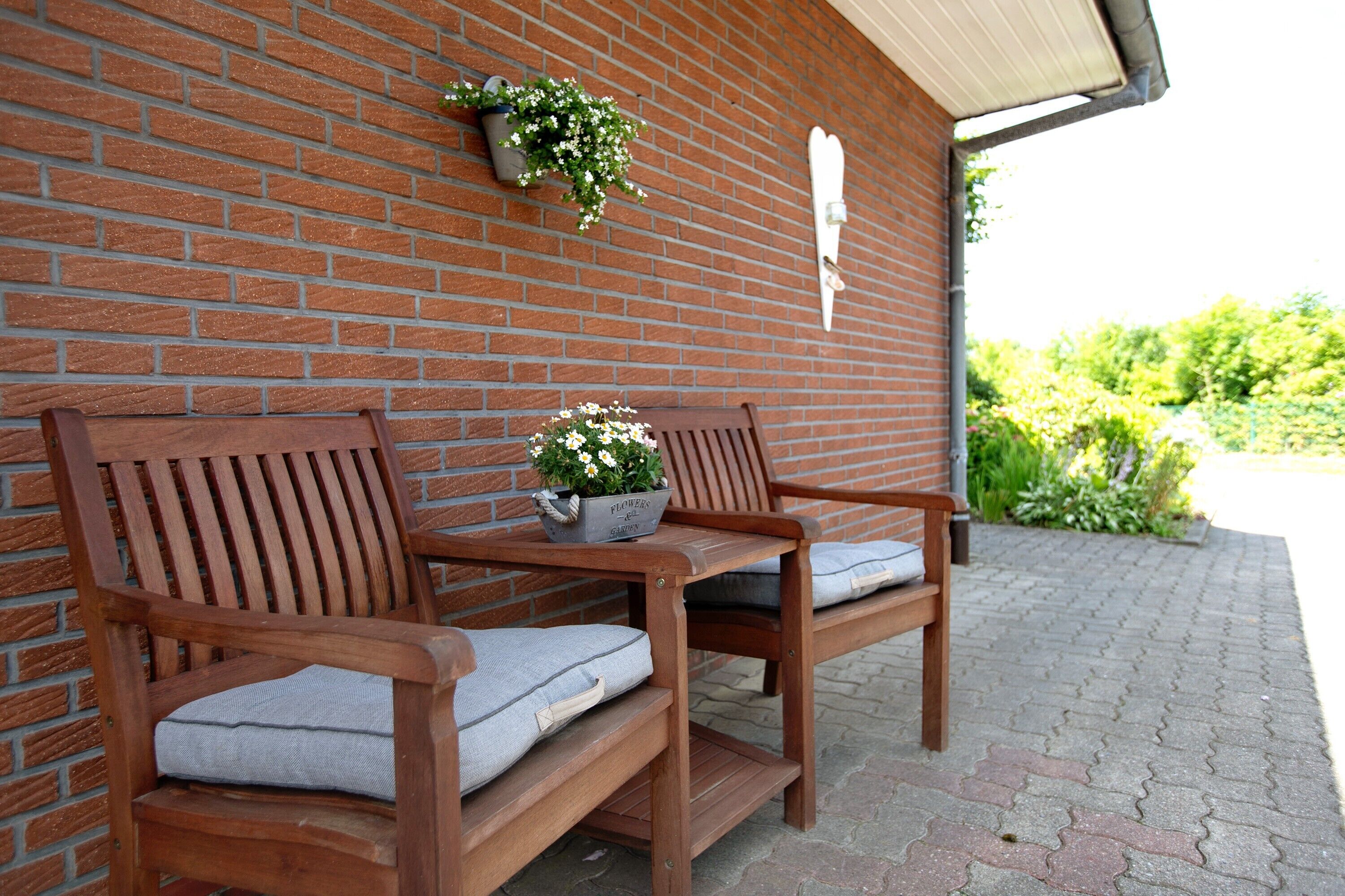 A wooden bench with cushions and a potted plant against a brick wall.