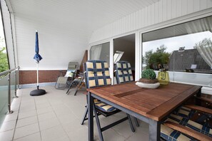 A covered patio area with a wooden table and chairs, a small potted plant, and a blue umbrella. - Apartment 'Große Ferienwohnung' with Shared Garden and Balcony (Nordstrand)