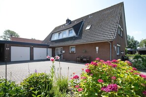 A residential building with a sloped roof, a garage, and a garden with flowers. - Apartment 'Große Ferienwohnung' with Shared Garden and Balcony (Nordstrand)