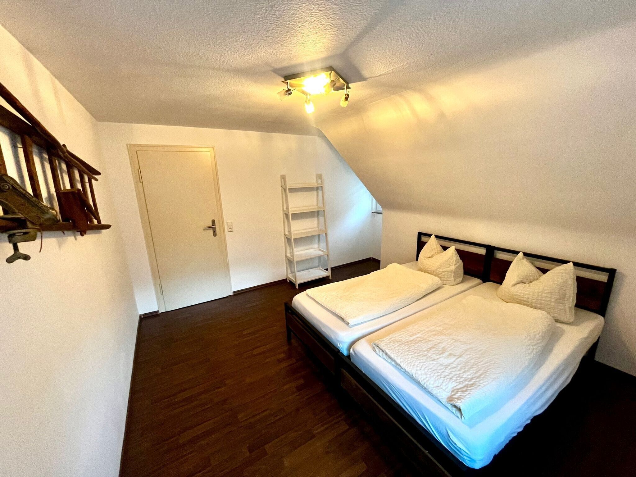 Een slaapkamer met een bed, een houten vloer, een witte deur en een plafondlamp.