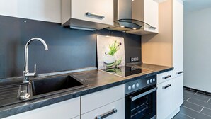A modern kitchen with a black countertop, stainless steel faucet, white cabinets, and a built-in oven. - Apartment 'Ferienwohnung Schwarzwaldliebe' with Private Terrace and Wi-Fi (Bad Peterstal-Griesbach)