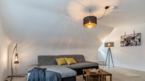 A modern loft bedroom with a sloped ceiling, a grey sectional sofa, a wooden coffee table, and a hanging light fixture. - Apartment 'Ferienwohnung Schwarzwaldliebe' with Private Terrace and Wi-Fi (Bad Peterstal-Griesbach)