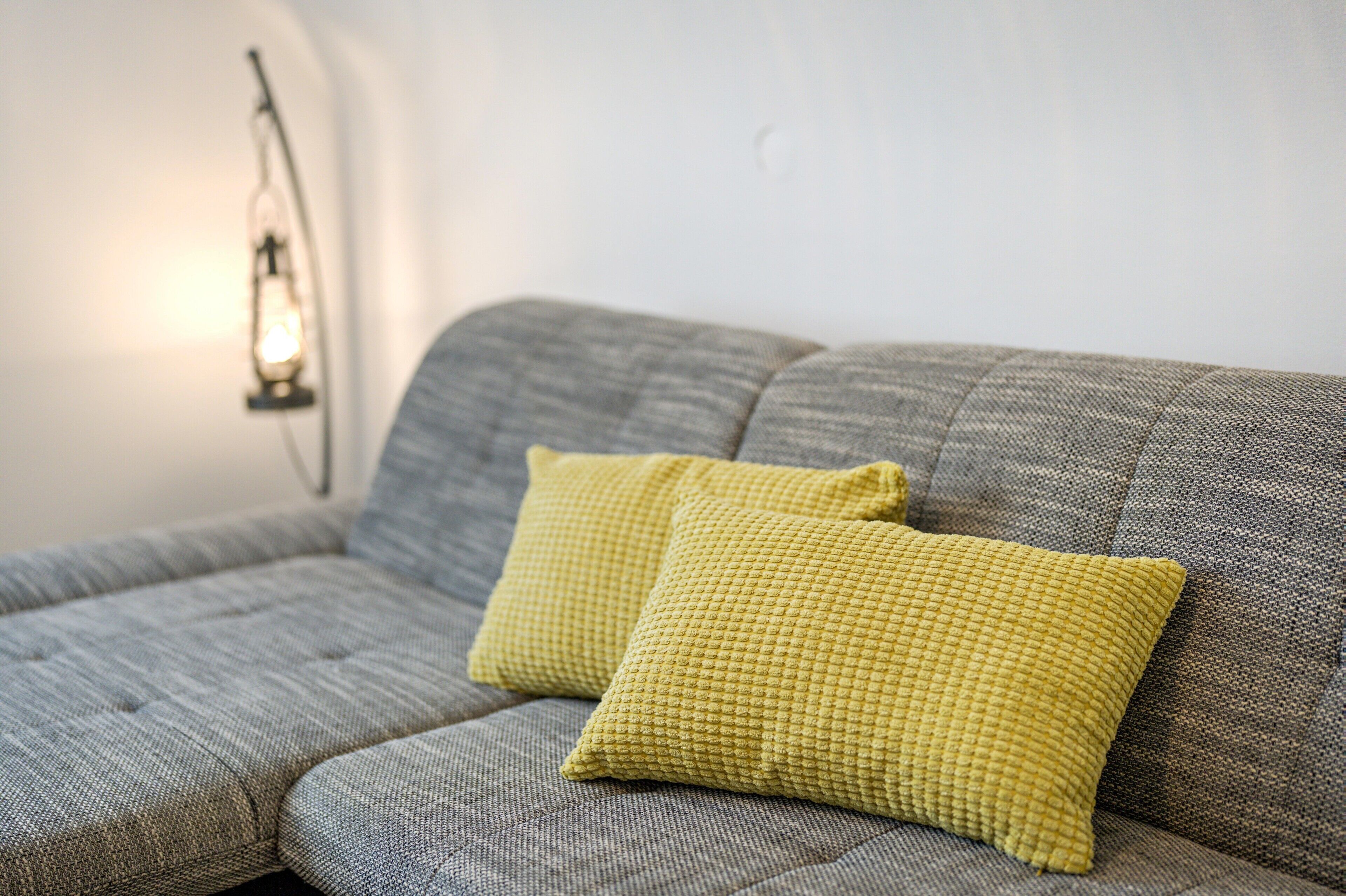A grey sofa with two yellow cushions and a wall-mounted light fixture.