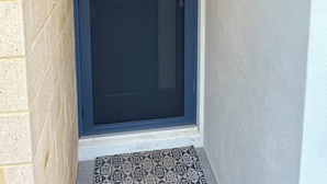 A dark-colored door with a glass panel, a small electronic device mounted on the wall, and a patterned mat at the entrance. - Seaside escape awaits your family in Myalup! (Myalup)
