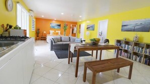 A bright living room with a sofa, a dining table, and a kitchen area with a stove. - ShineAwayHomes- Mountain view (Matavera District)
