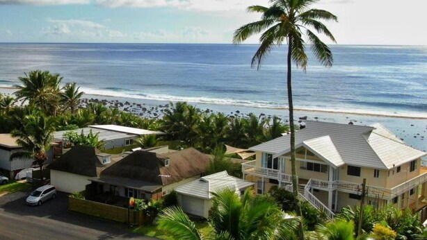 A coastal residential area with houses, a beach, and a palm tree. - ShineAwayHomes- Mountain view (Matavera District)