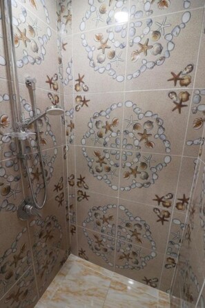 A shower area with a tiled wall featuring a seashell and starfish pattern.
