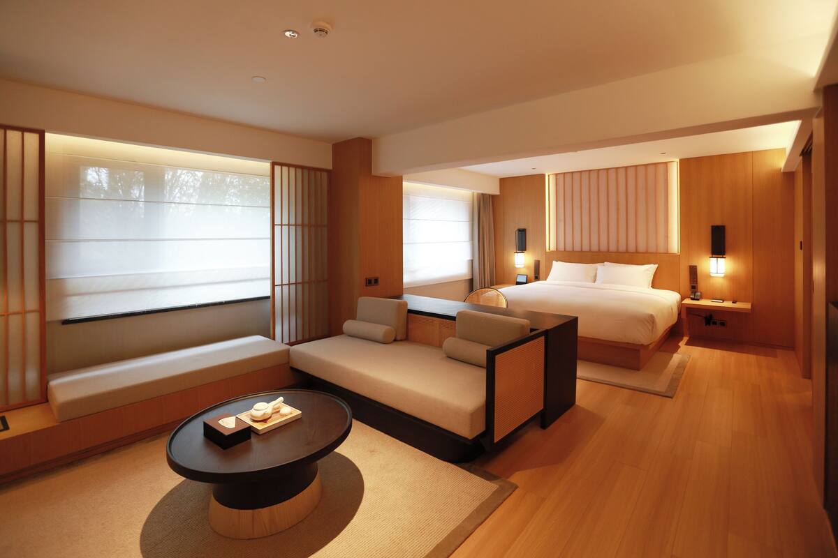Una habitación de hotel moderna con sofá, cama, mesa de comedor y un ventanal grande.