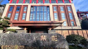 A traditional building with a red roof and columns, featuring large windows and a stone base with inscriptions.